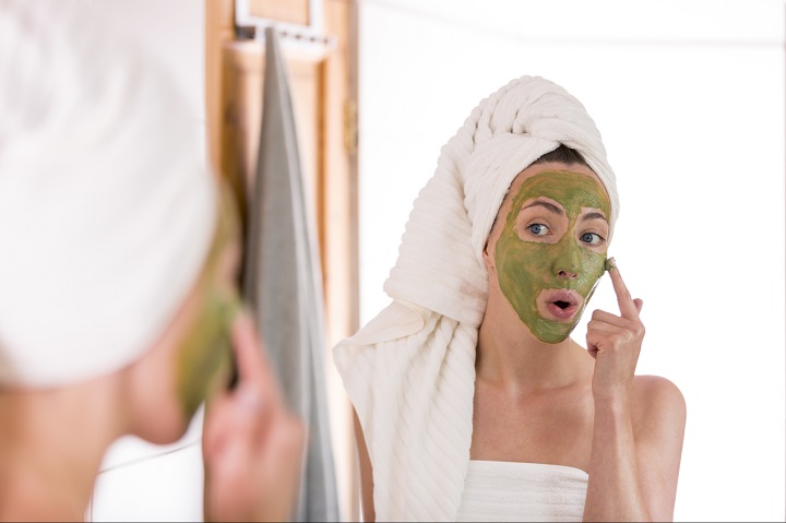 The woman applies green organic face mask in the bathroom