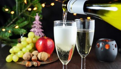 Pouring sparkling white wine in glasses on Christmas table. Christmas tree, lights and decorations in the background.