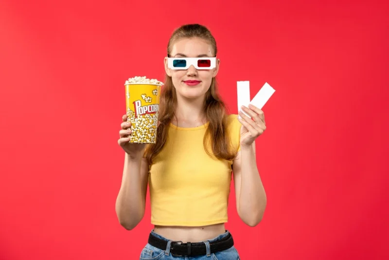young female at cinema holding popcorn package and tickets