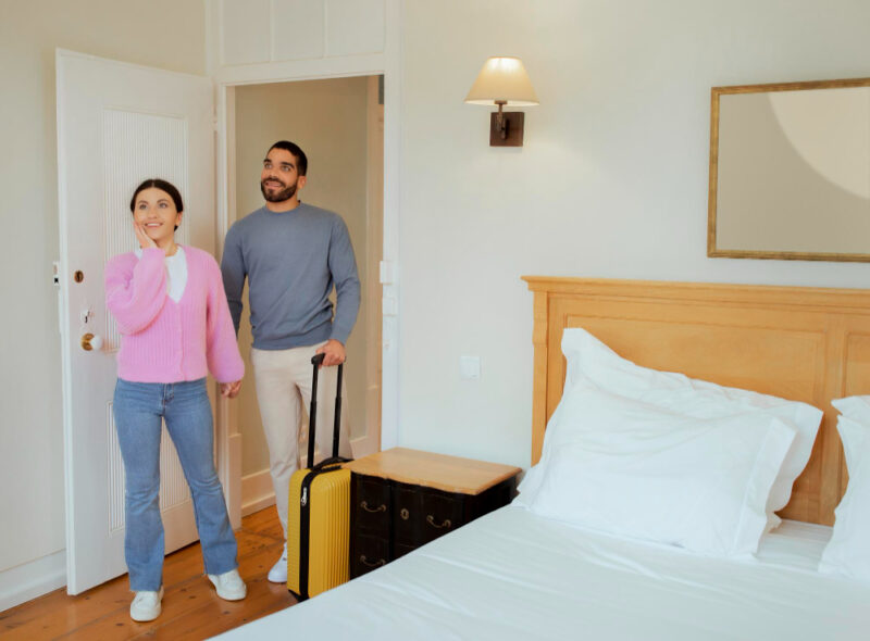 Couple Entering Hotel Room Standing With Suitcase Indoors
